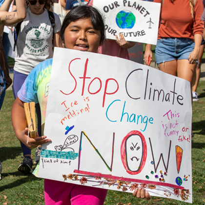 Photo of childing holding up sign for the environment that reads 'Stop Climate Change Now'
